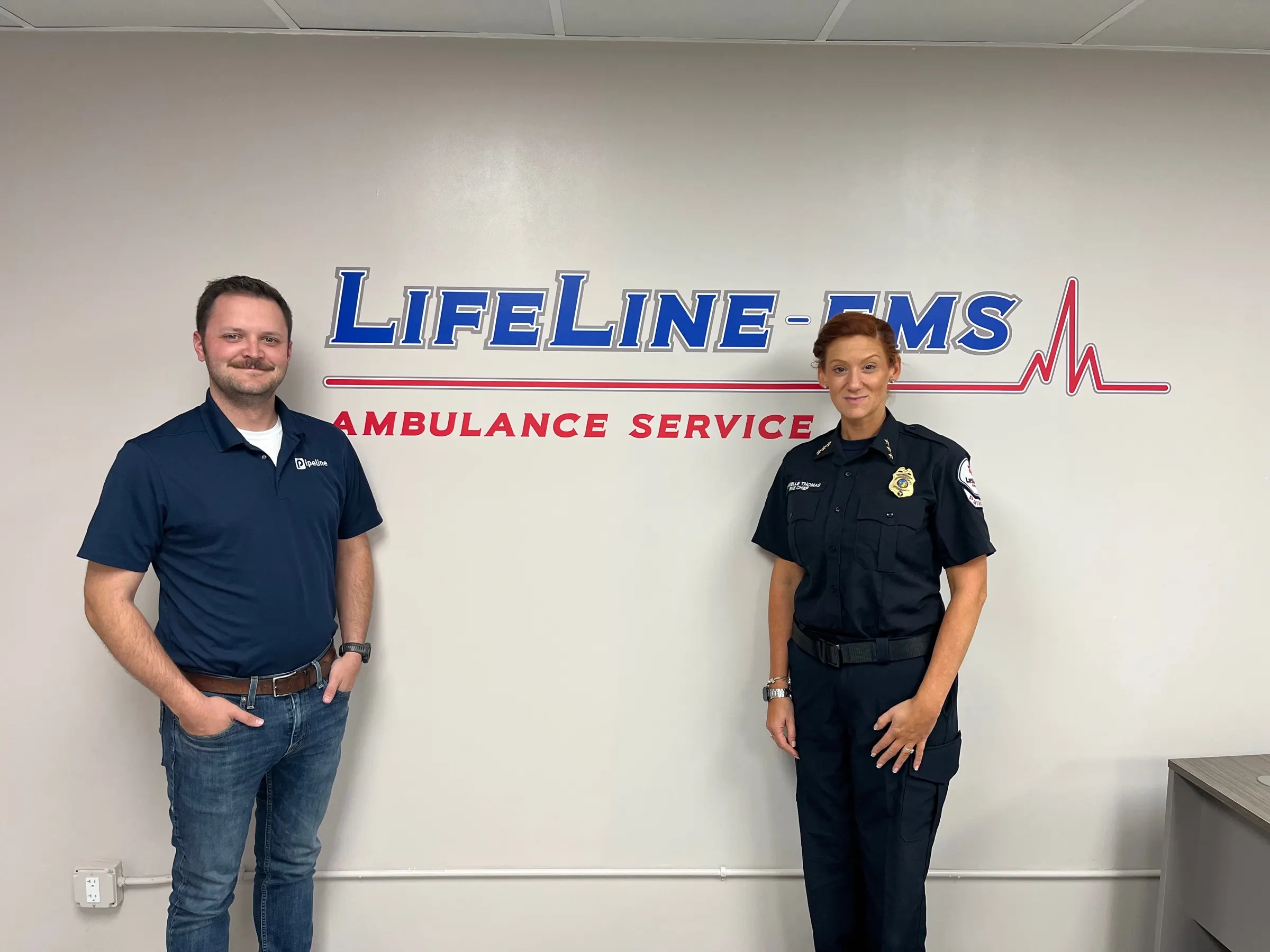 Pipeline on site with a training officer at a customer agency, in front of the agency wall sign.